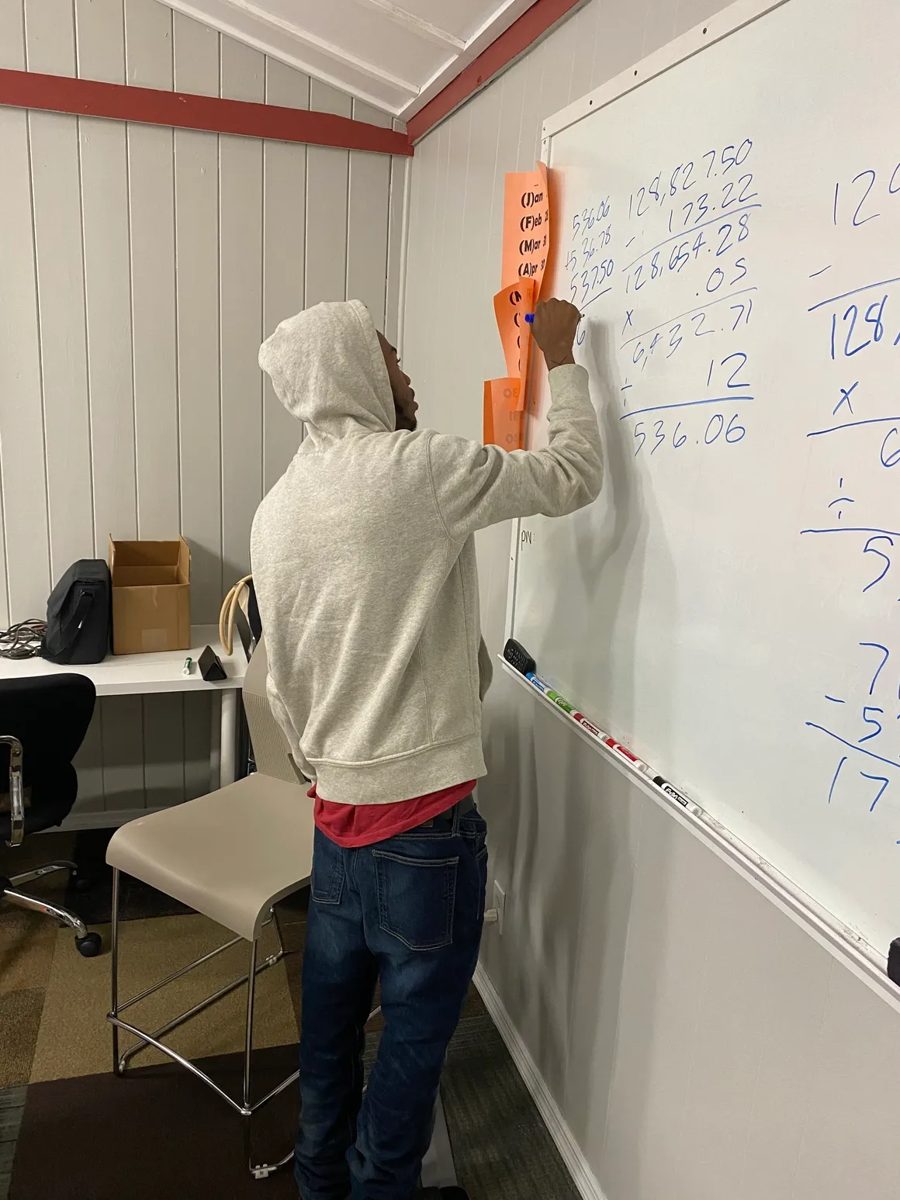 A student works a real estate math problem on the whiteboard